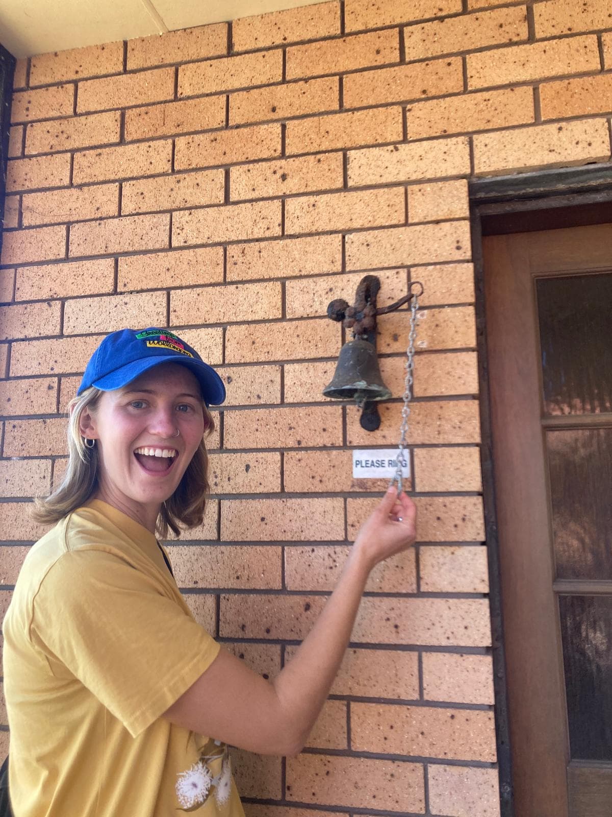 A volunteer at a front door, reaching for the bell beside a sign reading Please Ring
